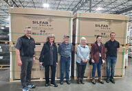 Six people stand in front of boxed solar panels in a warehouse building