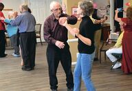 An elderly man dances with his middle-aged adult daughter
